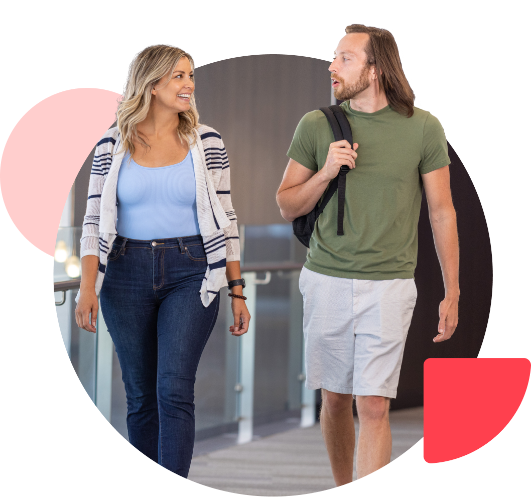 Two people smiling and talking as they walk down an office corridor.